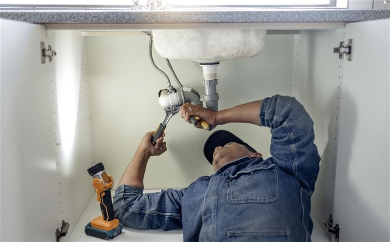 Plumber repairing pipes beneath a bathroom sink in Acworth