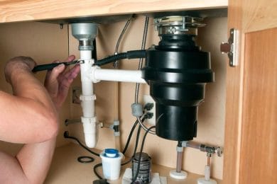Plumber repairing a garbage disposal beneath a kitchen sink in Acworth