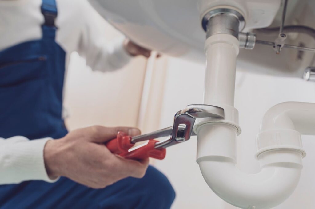 Plumber repairing a white drain pipe beneath a sink in Acworth