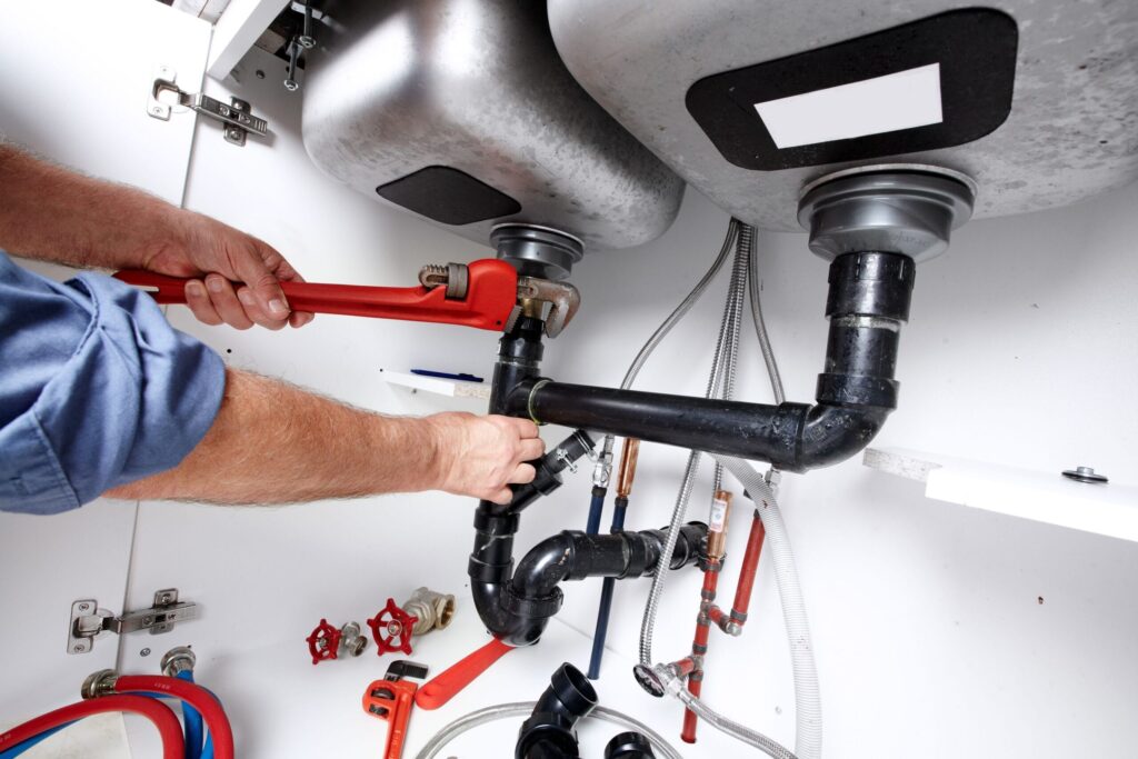 Plumber repairing drain pipes beneath a kitchen sink in Acworth